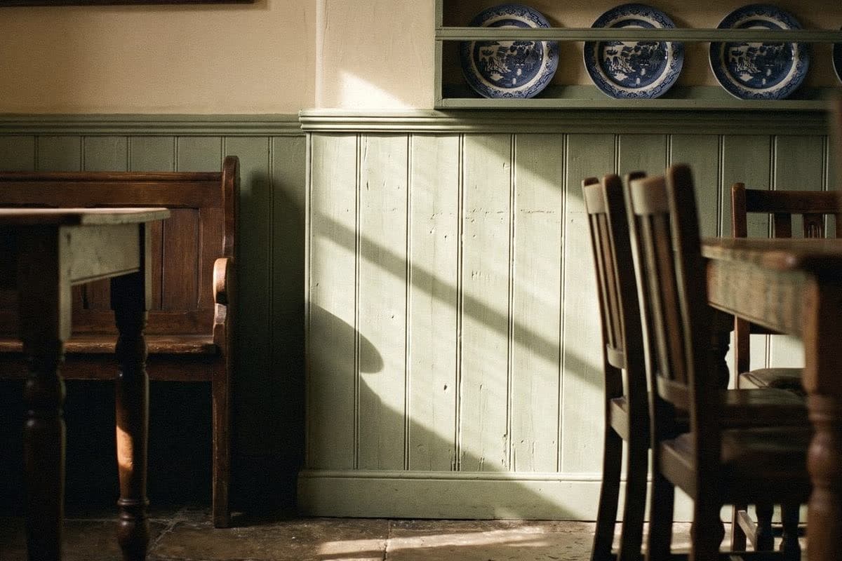 Sage green tongue-and-groove panelling with a shelf of blue-and-white plates, an old pew and wooden chairs