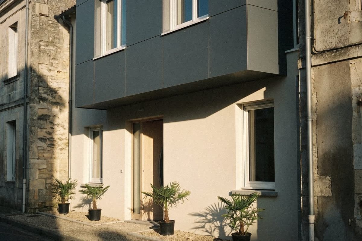 A cream house with a grey-panelled upper box, a pale wood door and potted palms along the front