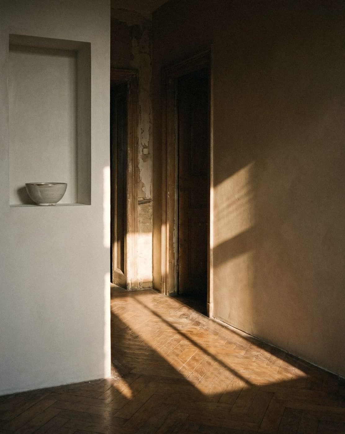 White wall niche holding a ceramic bowl, opening onto a hallway with a smooth warm beige wall and sunlit parquet